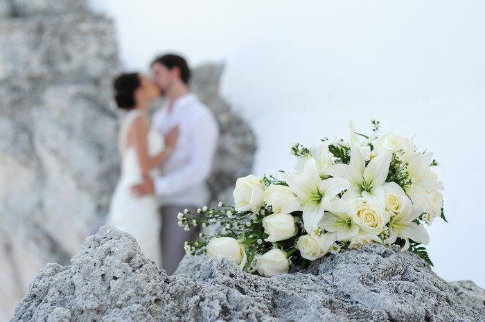 Wedding bouquet of roses and lilies on rocks with couple kissing