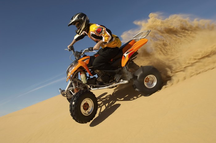 Man riding an orange ATV through sand dunes