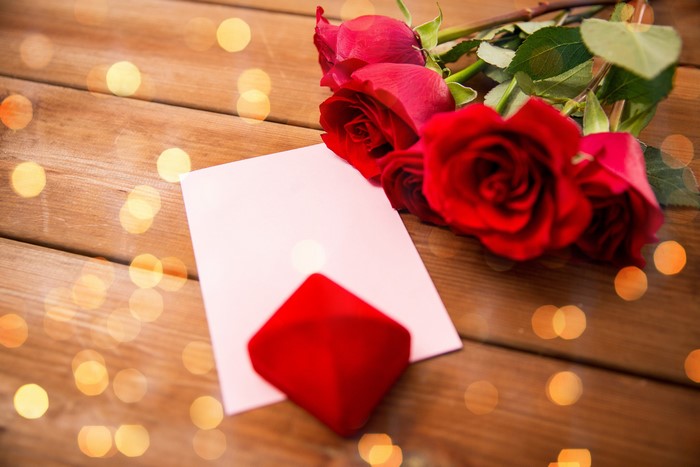Red roses, blank card, and ring box on wood