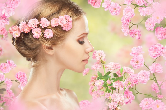 Blonde girl with pink flowers in hair smelling roses