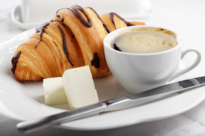 Croissant with chocolate drizzle, coffee, and butter on a plate