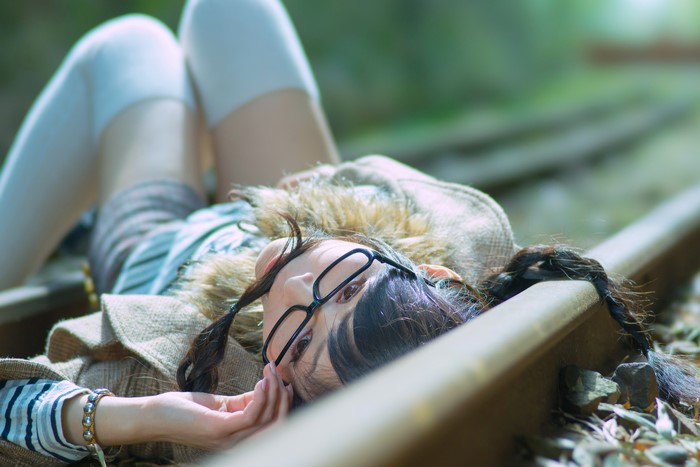 Brunette girl with glasses lying on railroad tracks