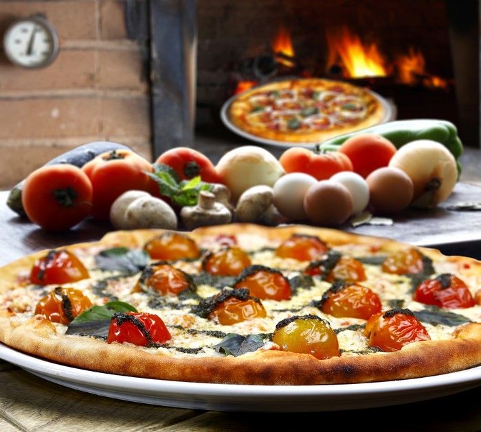 Pizza with tomatoes and basil near a pizza oven