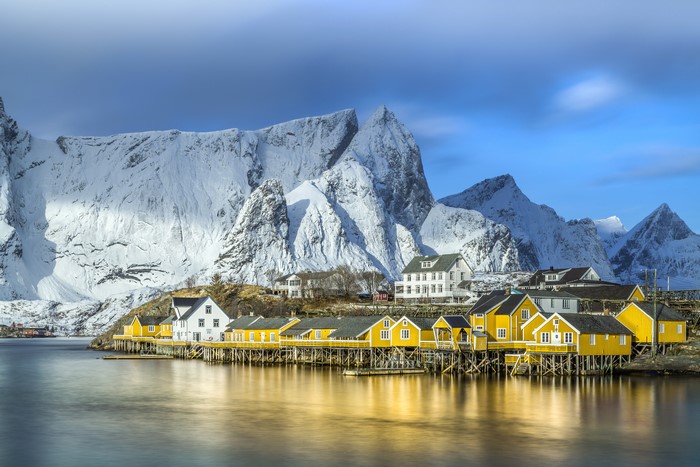 Yellow houses on stilts in Lofoten, Norway with snowy mountains