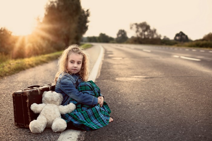Little girl with suitcase and teddy bear on the road