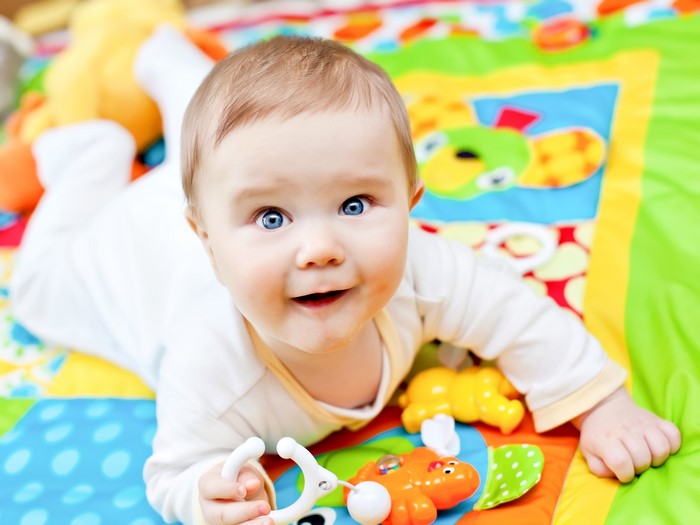Baby lying on a colorful playmat with toys