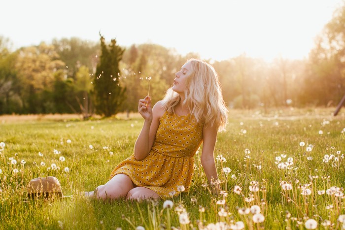 Blonde girl blowing dandelion seeds in a field