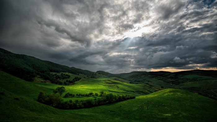 Rolling green hills under stormy clouds