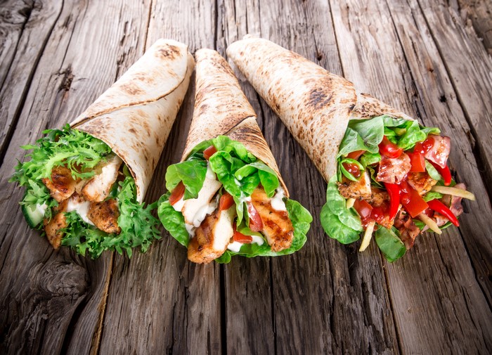 Three chicken wraps with vegetables on a wooden table