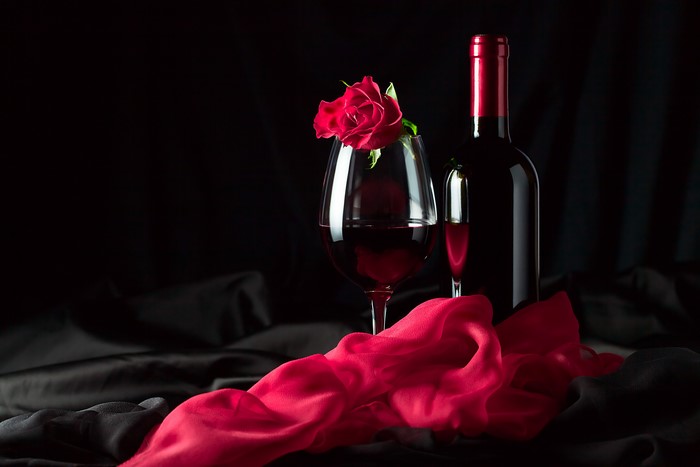 Wine bottle, wine glass, and red rose on black background