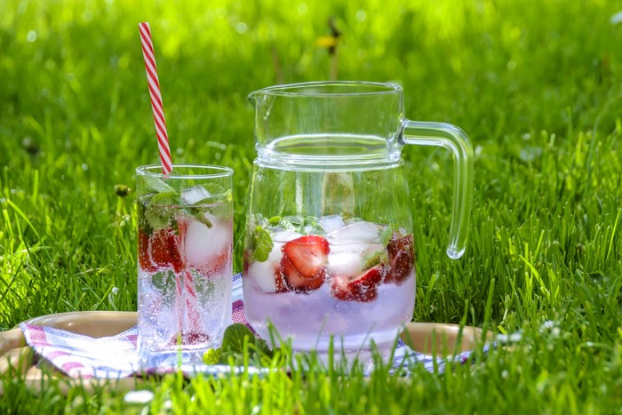 Strawberry mint infused water in a glass and pitcher on grass