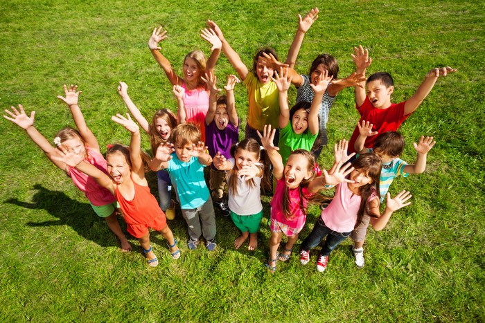 Group of happy children with hands raised on grass