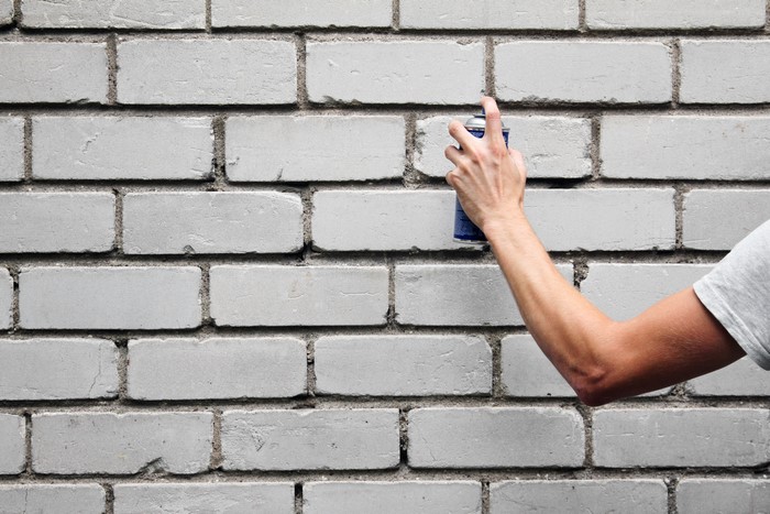 Hand holding spray can against brick wall