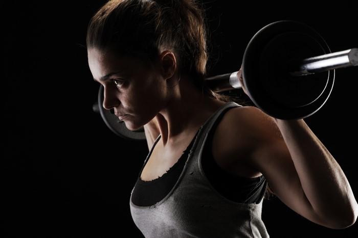 Woman lifting barbell on black background