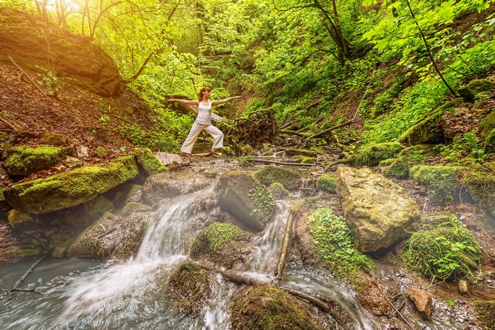Woman doing yoga by a waterfall in a forest