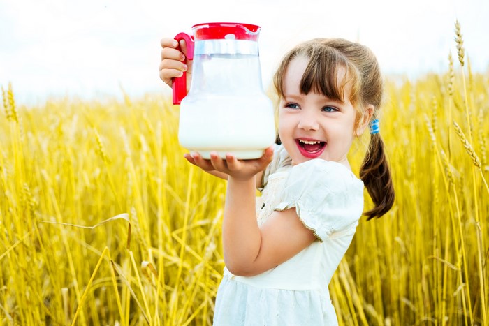 Little girl holding a jug of milk in a wheat field