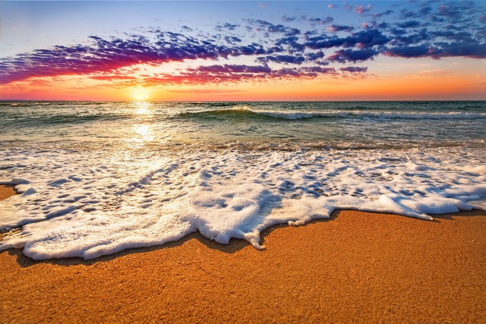 Sunset over the sea with foamy waves on the shore