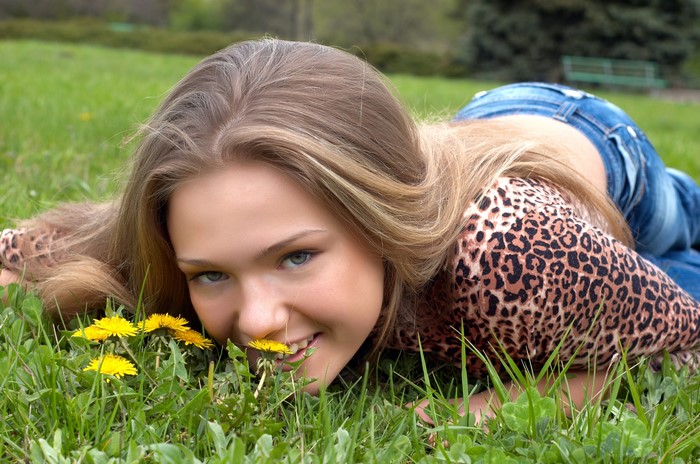 Young woman with blonde hair lying in grass with dandelions