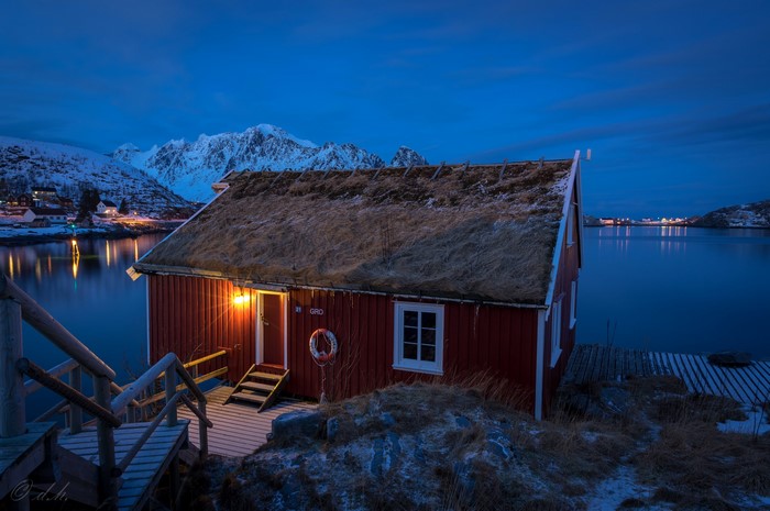 Red house with grass roof by a lake at night in Reine, Norway