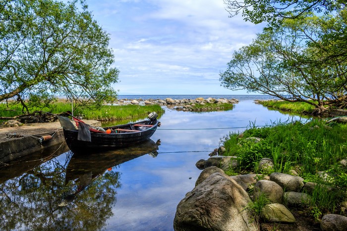 Boat moored in a narrow river inlet with trees and sea in background