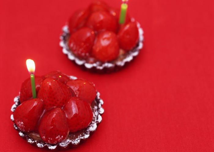 Two strawberry tarts with candles on red background