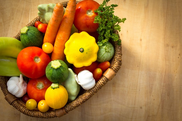Basket of fresh vegetables including carrots, tomatoes, and garlic