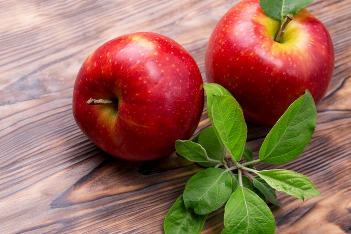 Two Red Apples with Leaves on Wood