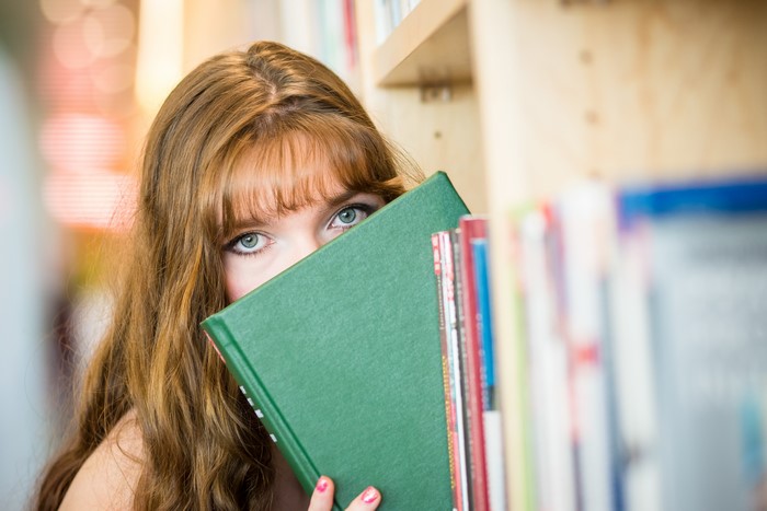 Brown haired girl peeking over a book