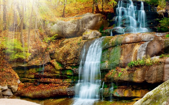 Waterfall in an autumn forest with sun rays