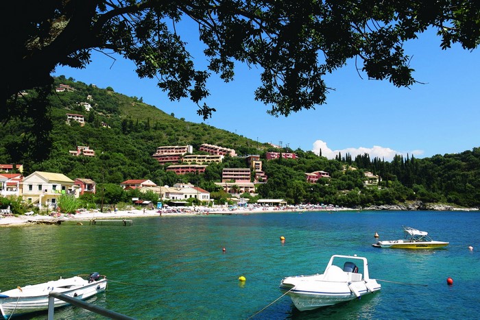 Boats in a bay with houses on a green hill in Corfu, Greece