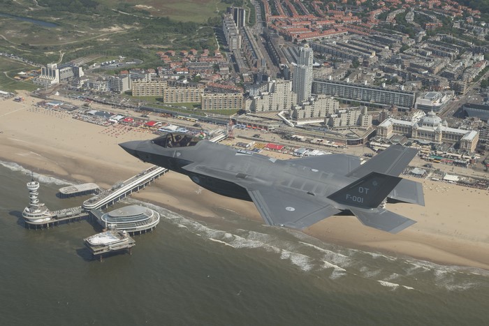 F-35 Lightning II fighter jet flies over a beach and city