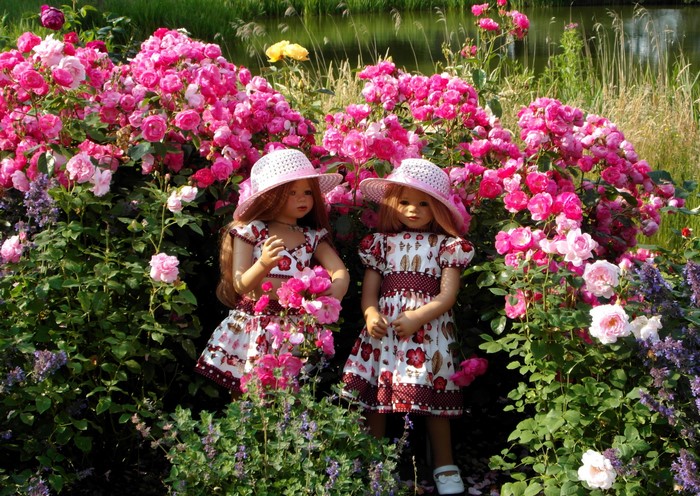 Two dolls in dresses and hats in a rose garden