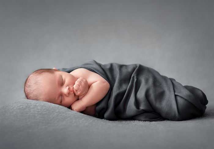 Newborn baby sleeping wrapped in a dark grey swaddle