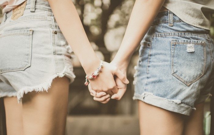 Two people holding hands, wearing denim shorts