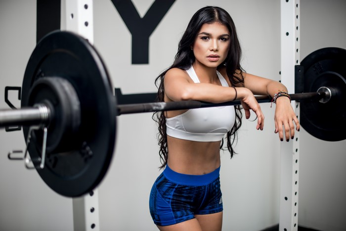 Brunette girl leaning on barbell in gym