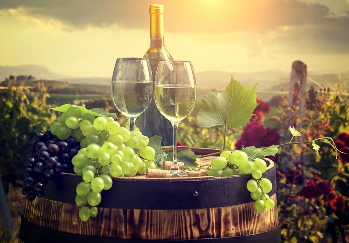 Wine bottle and glasses on barrel with grapes