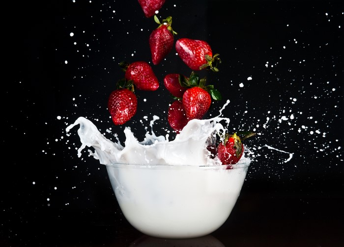 Strawberries splashing into milk on black background