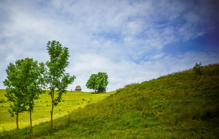 Two small houses on a grassy hill under a cloudy sky