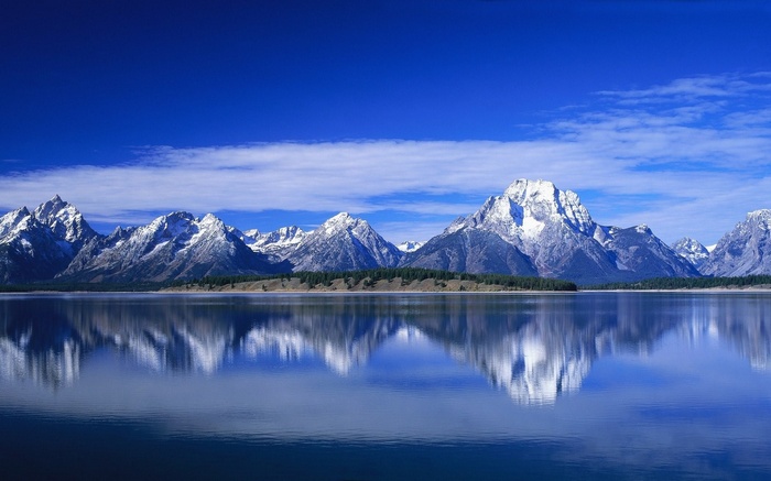 Snow-capped mountains reflected in a calm lake under a blue sky
