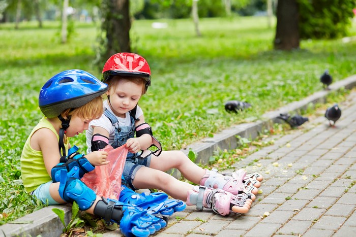 Two children in helmets and protective gear sitting on grass