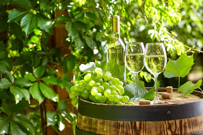 White Wine Bottle and Glasses with Grapes on Barrel