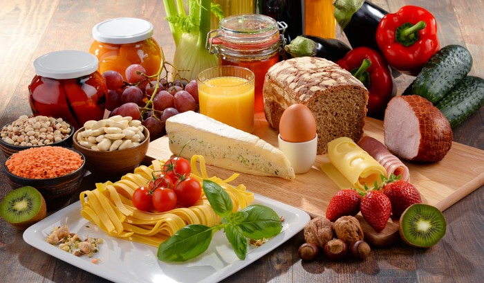 Still-life of food including bread, cheese, ham, and fruits