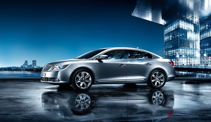 Silver Buick LaCrosse parked by a city skyline at night
