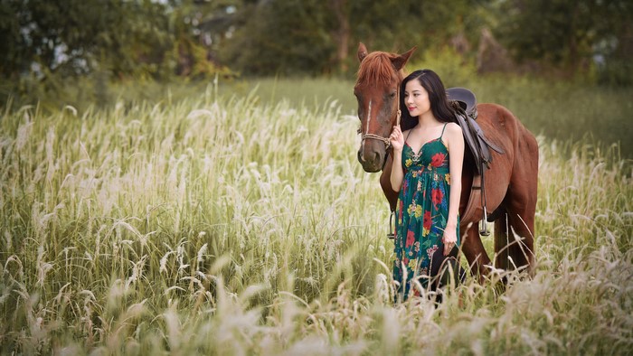 Asian woman with horse in grassy field