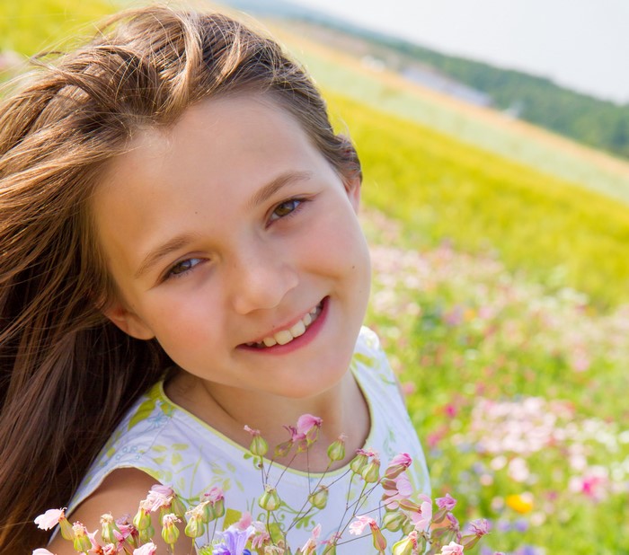Young girl with brown hair smiling in a field of flowers