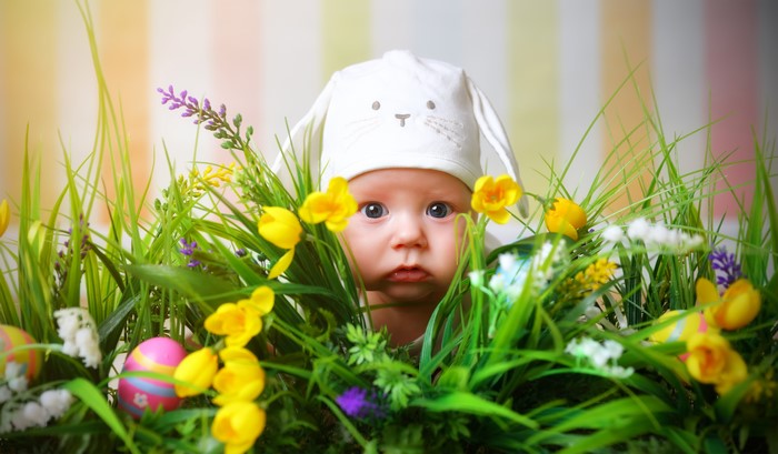 Baby in bunny hat among Easter eggs and flowers