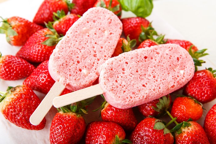 Two strawberry ice pops with fresh strawberries