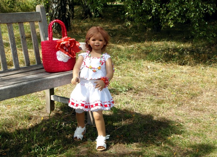 Doll in a white dress with a red handbag on a bench