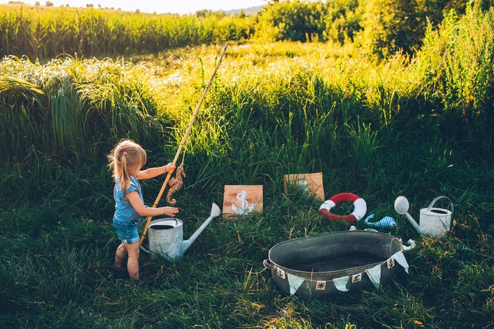 Girl fishing with toy seahorse in a field