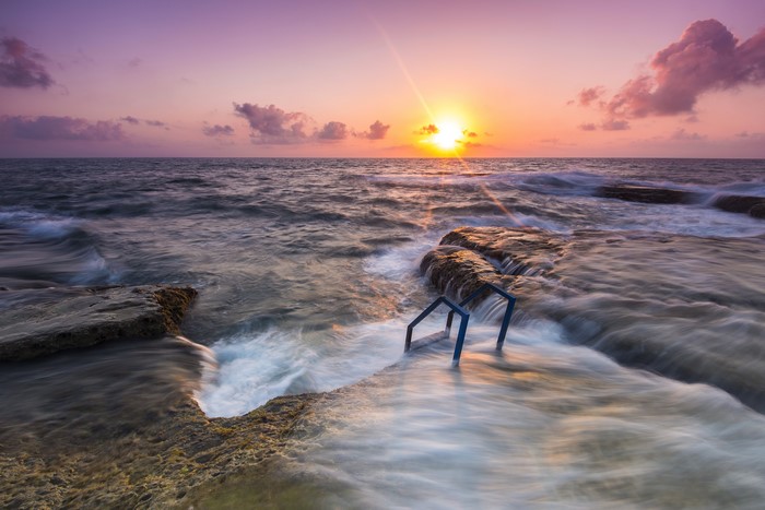Sunrise over the sea with rocky shore and ladder